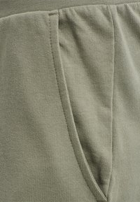 Detailní pohled na světle zelenou pletenou kapsu s viditelným švem a detaily elastického pasu.