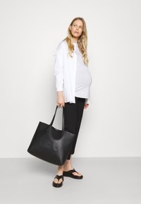 Bolsa tote preta em pele com textura suave, alças duplas, grande abertura no topo, combinada com uma blusa cinza, camisa branca e calças pretas.