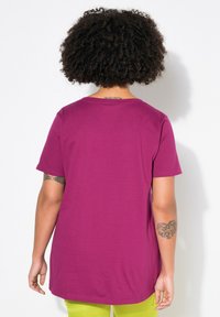 Magenta bomulds t-shirt med korte ærmer og rund hals. Stoffet er glat med en let afslappet pasform. Synlige tatoveringer på armene.