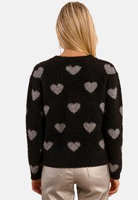 Maglione nero peloso con motivi a cuore argento, colletto a coste e maniche lunghe. Texture visibile con una finitura morbida e soffice.