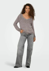 Pull en tricot à col en V de couleur gris clair, associé à un jean gris à jambes larges, tous deux présentant une coupe décontractée et un tissu texturé. Des chaussures noires viennent parfaire la tenue.