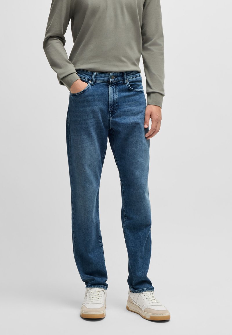 Dark blue denim jeans with a straight cut, five-pocket design, and a light fade. Paired with a grey long-sleeve shirt and white sneakers.