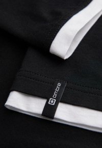 Černobílá vrstvená tkanina s černou etiketou označenou "ombre", zašitou blízko okraje černé vrstvy tkaniny.