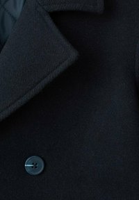 Cappotto in lana nera con colletto a revers e chiusura con un singolo bottone blu, realizzato in tessuto morbido e strutturato dal design elegante.