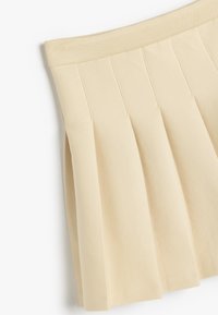 Mini falda plisada en tela beige con una cinturilla suave y elástica. La textura es suave, con pliegues verticales para un detalle adicional.