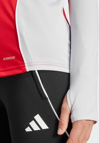 Rød og hvid atletisk langærmet trøje med mesh tekstur og tommelhul, parret med sorte bukser med hvid stribe og Adidas-logo.