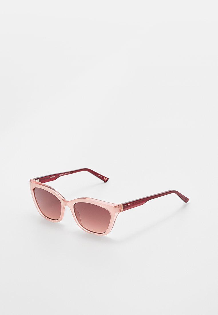 Pink cat-eye sunglasses with gradient brown lenses and red arms resting on a white surface.