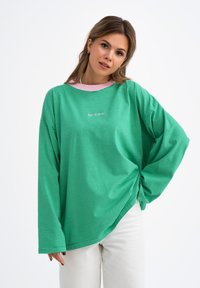 Groen gestreept overhemd met lange mouwen en een losse pasvorm, voorzien van een roze kraag en subtiele logo-detail aan de voorkant. Gemaakt van een katoenmix.