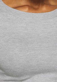 Canottiera in cotone grigia con una texture a coste, dotata di un ampio scollo. Il tessuto ha una qualità morbida ed elastica, che mette in risalto la forma del corpo.