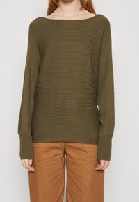Olive green ribbed sweater with a wide boat neck and long, fitted sleeves. Paired with light brown pants, showing a relaxed fit.