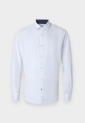 Chemise blanche à manches longues avec boutons, motif subtil de points bleus et col intérieur bleu marine avec de petits losanges blancs.
