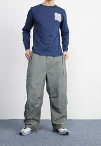 Mörkblå långärmad t-shirt med vit grafik på bröstfickan, i kombination med lösa, ljusgrå cargobyxor med sidofickor.