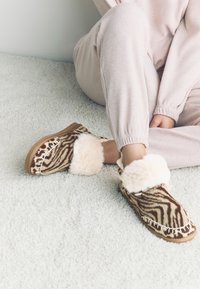 Chaussons à motif zèbre marron en fausse fourrure douce, avec un bord en peluche crème et une semelle texturée avec des détails de coutures apparentes.