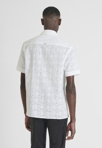 Witte shirt met korte mouwen en een gestructureerd bloemen uitsnijdpatroon, voorzien van een kraag en een knoop aan de achterkant, gemaakt van ademende stof.