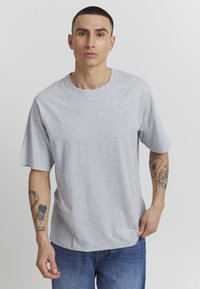 Gray short-sleeve t-shirt with a round neck, made of cotton; worn by a person with tattoos on their forearm. Simple and casual design.