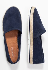 Espadrilles slip-on in suede blu navy con dettagli in giunco intrecciato e suola in gomma bianca. Presentano una texture liscia e un design minimalista.
