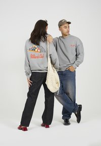 Felpe grigie con grafica "Billiards Club", jeans di denim e una borsa a tracolla intrecciata. Le calzature includono scarpe con tacco rosso e scarpe nere.