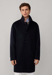 Cappotto di lana navy con colletto alto, chiusura a cinque bottoni e due tasche laterali, con taglio dritto e texture morbida.