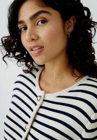 Gestreifte Strickjacke in Creme und Navy, mit rundem Ausschnitt, Knopfverschluss und strukturierter Strickware. Akzente bilden glänzende Knöpfe.