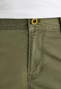 Olivgrüne Baumwollhose mit glatter Textur, ausgestattet mit einem gelben und schwarzen Knopf an der Taille und dezenten Nähdetails.