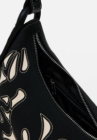 Borsa a mano in tessuto nero con un design testurizzato e dettagli beige, dotata di chiusura con zip e tasca interna supplementare.
