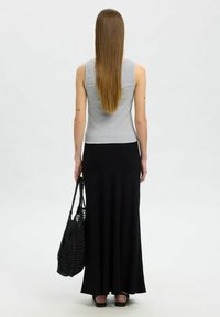 Débardeur gris à côtes avec un design ajusté, associé à une longue jupe noire. Le modèle tient un sac en crochet noir. Les cheveux sont longs et raides.
