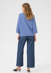 Haut bleu ample à manches trois-quarts, associé à un pantalon en denim à jambes larges avec un ourlet roulé et des mules noires à talons.