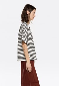 T-shirt à rayures à manches courtes en noir et blanc cassé, avec une coupe décontractée et un col rond. Tissu doux avec une texture subtile.