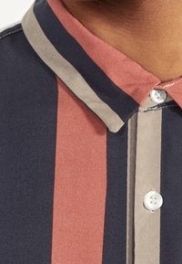 Koszula z krótkim rękawem z pionowymi paskami w kolorach granatowym, beżowym i różowym. Z kołnierzykiem i zapinana na guziki, wykonana z tkaniny tkanej.