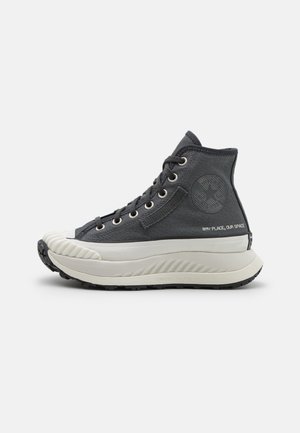 Baskets montantes en tissu gris foncé avec une semelle blanche. Présentent un capuchon de protection texturé, des œillets en métal et un logo sur le côté.