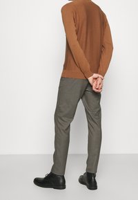 Maglione marrone a maglia con schiena testurizzata, abbinato a pantaloni grigi a scacchi e scarpe nere con stringhe, visto da dietro.