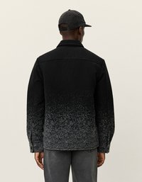 Schwarze Wolljacke mit einem grauen Farbverlauf, knöpfbarem Vorderteil und langen Ärmeln. Person trägt eine gemusterte schwarze Mütze, von hinten betrachtet.