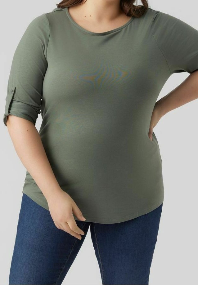 Top verde oliva a maniche corte con scollatura rotonda e risvolti; tessuto morbido e liscio con leggero elastico. Abbinato a jeans blu.