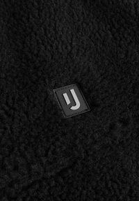 Fekete, texturált polár anyag, négyzet alakú, fekete gumi folttal, amelyen egy fehér, stilizált 'J' logó látható. Puha, meleg megjelenés.