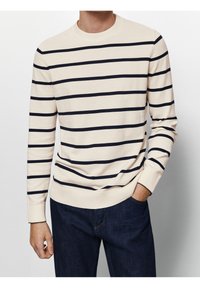 Cremfarbener Pullover mit navyblauen horizontalen Streifen, Rundhalsausschnitt, gerippten Bündchen und Saum, kombiniert mit dunkelblauen Denim-Jeans. Weicher, leichter Strickstoff.