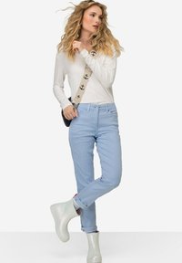 Jasnoniebieskie dżinsy o slim fit, zestawione z białą bluzką z długim rękawem i irydyscencyjnymi kaloszami. W zestawie znajduje się torba na pasek z wzorem.