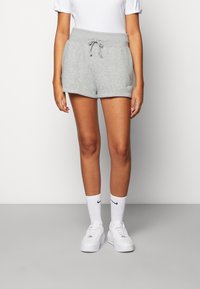 Pantalones cortos de algodón grises con cintura elástica, cordón y logo bordado. Llevados con calcetines blancos y zapatillas. Diseño sencillo y casual.