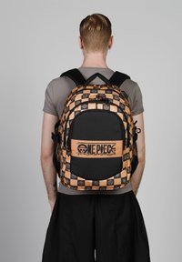 Mochila a rayas en negro y naranja con logotipo. Cuenta con correas ajustables, un gran bolsillo frontal y tela texturizada con detalles gráficos.