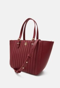 Rote Handtasche aus Kunstleder mit vertikal geripptem Design, goldfarbenen Beschlägen, zwei oberen Griffen und einem verstellbaren Schultergurt.