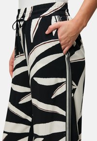 Pantaloni bianco e nero con un motivo a foglia, dotati di un elastico in vita, tasche laterali e dettagli a strisce in contrasto.