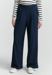 Wijdvallende broek in donker marineblauw, gemaakt van een zachte stof. Heeft een hoge elastische tailleband en subtiele voorplooien voor structuur.
