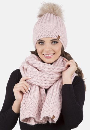 Beanie rosa lavorato a maglia con pompon in pelliccia e sciarpa abbinata. Entrambi presentano un motivo testurizzato e sono leggeri, accoglienti e caldi.