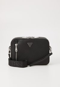 Bolso de cuero negro texturizado con cierre de cremallera, herrajes plateados y una correa de tela con el logotipo "GUESS". Diseño compacto rectangular.