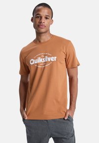 Kurzärmliges T-Shirt mit Rundhalsausschnitt aus burnt orange Baumwolle, das ein großes weißes Quiksilver-Logo auf der Brust und eine glatte Textur aufweist.