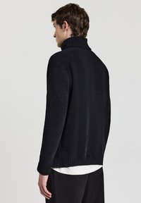 Maglione nero in maglia spessa con colletto alto, polsini e orlo a costine, caratterizzato da un tessuto testurizzato e una vestibilità rilassata.