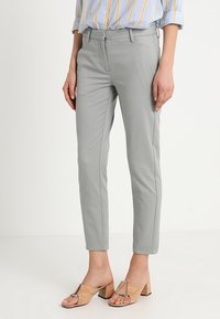 Grijze broek tot de enkels van een gestructureerde stof, slim fit, met zijzakken en een platte voorkant. Gecombineerd met tan block-heel sandalen.