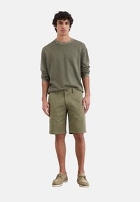 Pull vert olive et shorts, en coton, col rond, coupe décontractée, associé à des chaussures beiges. Design simple sans motifs.