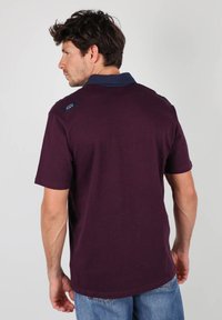 Polo shirt à manches courtes de couleur violet foncé avec un col en marine contrastant, présentant un petit logo sur la partie supérieure du dos.