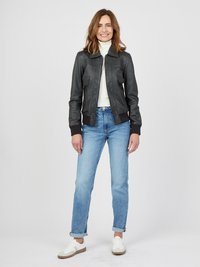Svart läderjacka med framdragkedja, räfflade ärmar och krage; kombinerad med ljusblå jeans och vita sneakers. Slät textur, skräddarsydd passform.