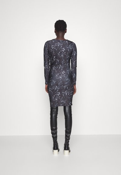 Čierne dlhé šaty s mramorovým bielym vzorom, priliehavý strih, po kolená. V kombinácii s čiernymi vysokými čižmami po kolená.